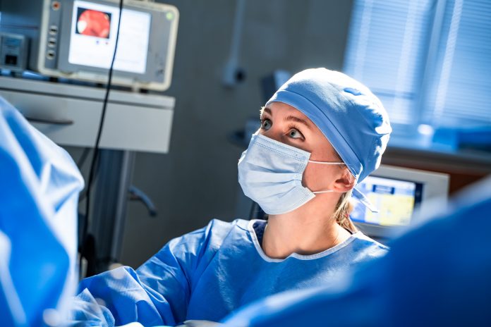 Portrait of the professional nurse medical assistant in surgical mask during operation. Modern hospital operating room.